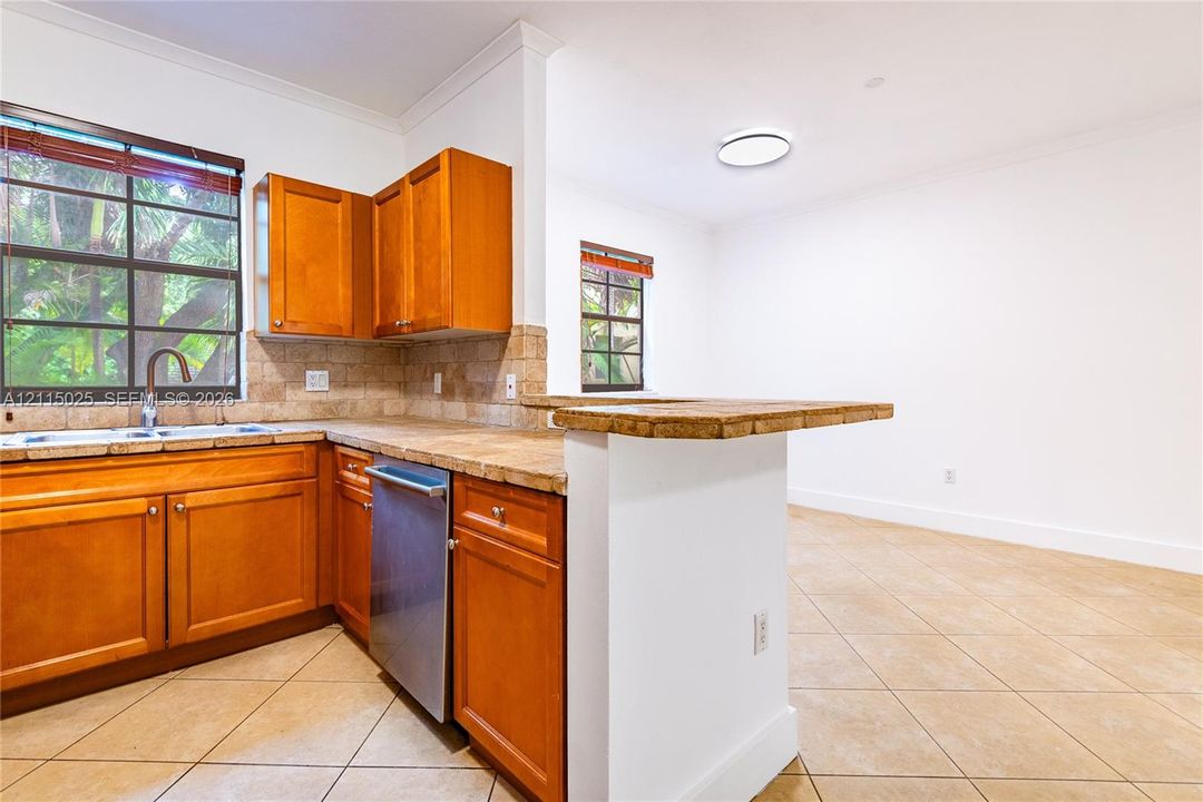 Kitchen featuring wood cabinetry, stone tile countertops, tiled backsplash, stainless steel dishwasher, and tile flooring