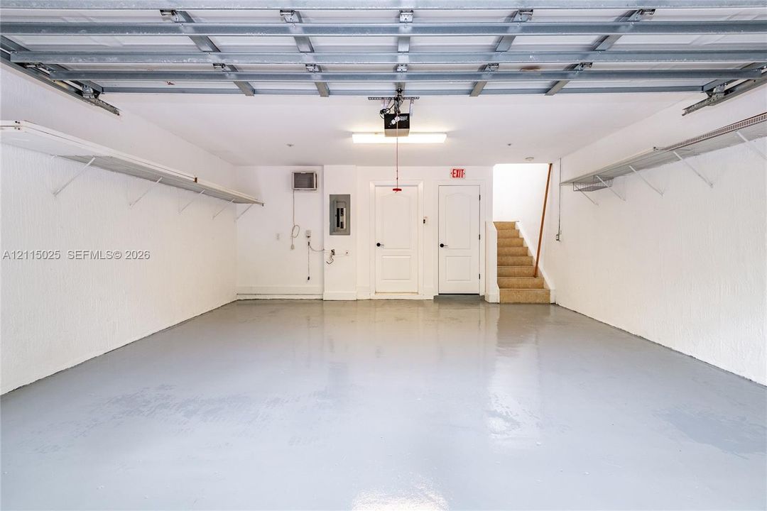Garage featuring an epoxy-coated floor, built-in wall shelving, dual entry doors, and overhead lighting