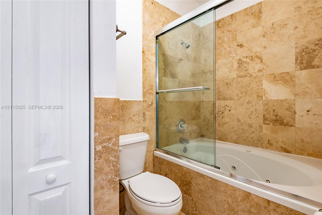 Jetted soaking tub with chrome fixtures, sliding glass enclosure, and stone tile surround