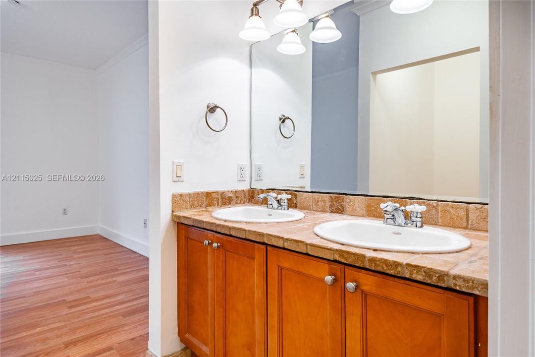 Double vanity featuring wood-finish cabinetry, natural stone tile countertop, dual undermount sinks, and wall-to-wall mirror with four-light fixture