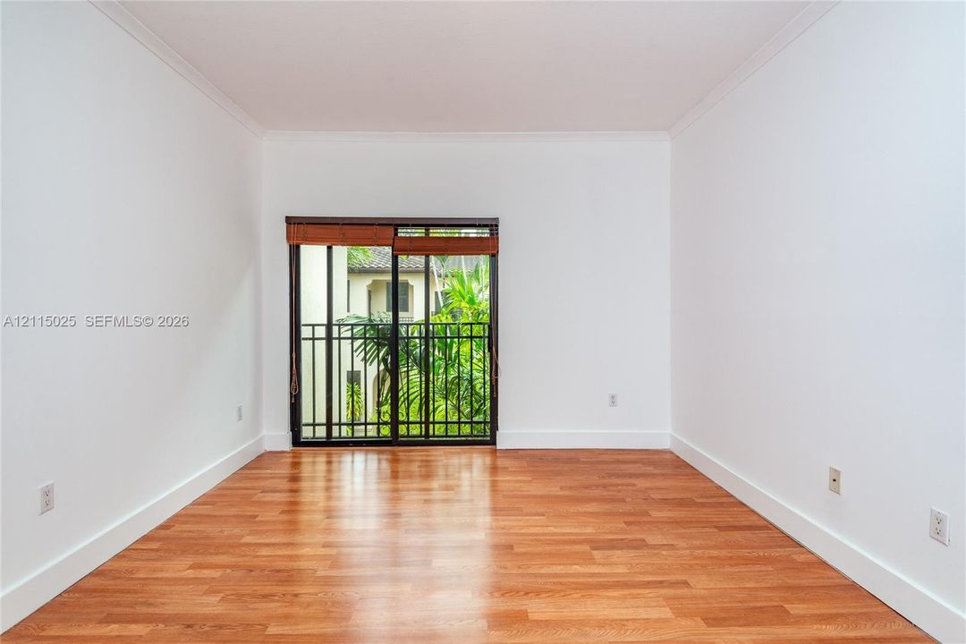 Interior room featuring wood-finish flooring, white walls, crown molding, and a sliding glass door providing egress to a metal-railed balcony