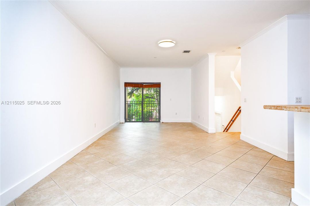 Neutral interior featuring diagonal tile flooring, smooth wall finishes, crown molding, and a sliding glass door providing access to a railed balcony