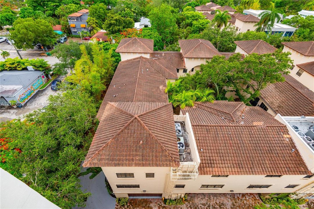 Aerial perspective of a multi-level structure featuring a multi-pitched tile roof and masonry exterior, accented by mature canopy trees and established landscaping