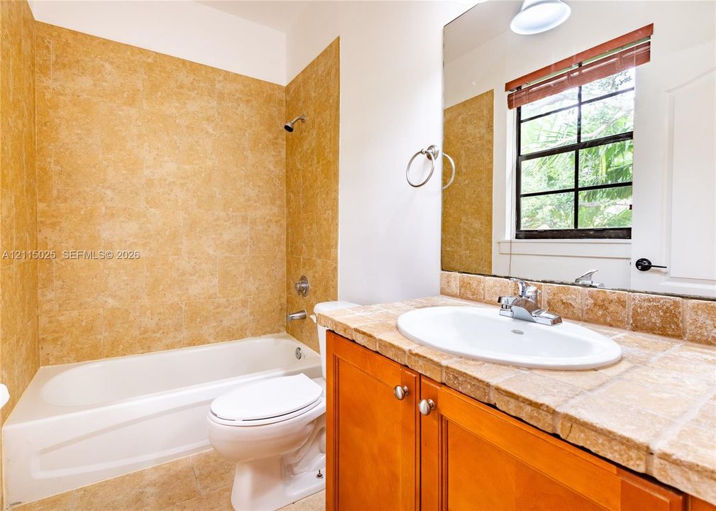 Bathroom featuring a vanity with a tiled countertop, drop-in basin, wood-finish cabinetry, a large wall-mounted mirror, and a tub-shower combination with floor-to-ceiling tile surrounds