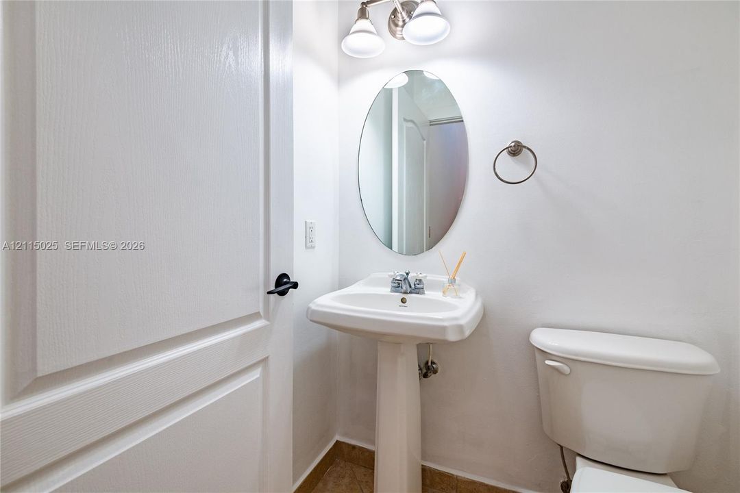Pedestal sink with chrome faucet, oval wall-mounted mirror, two-light fixture, and circular towel ring