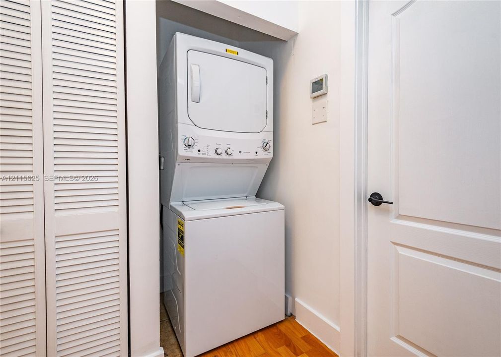 Stacked white laundry unit featuring a top-load washer and dryer, louvered closet doors, and wood-finish flooring