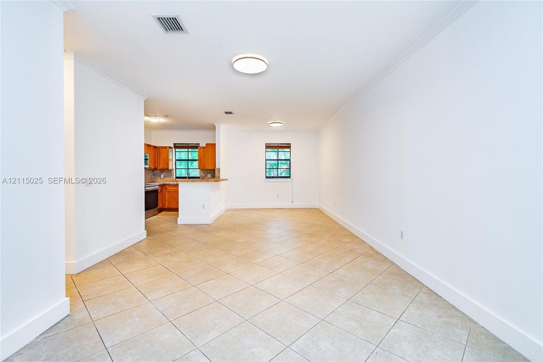 Open-concept interior featuring neutral tile flooring, recessed ceiling lighting, crown molding, and wooden cabinetry with an integrated breakfast bar