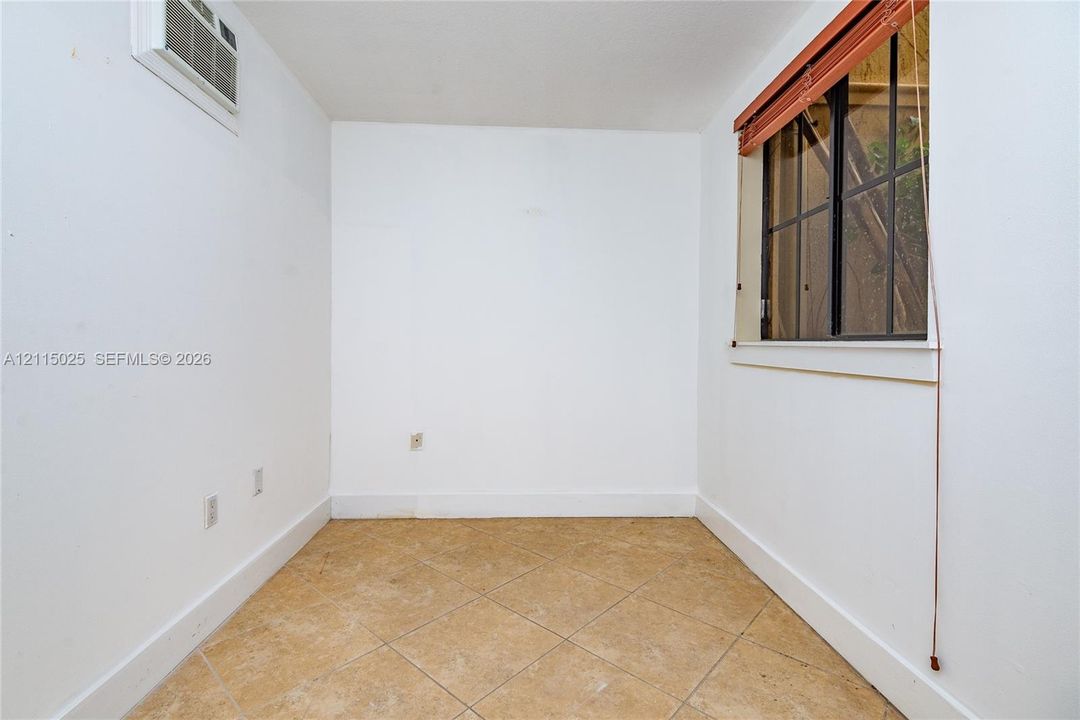 Interior space featuring tile flooring in a diagonal pattern, a window with a brown-finish blind, and an integrated wall-mounted air conditioning unit