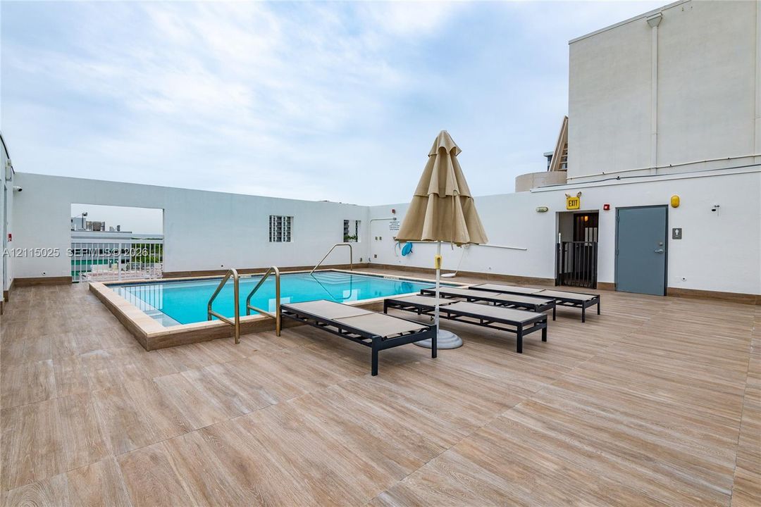 Rooftop swimming pool featuring wood-finish tile decking and metallic handrails, enclosed by a perimeter wall