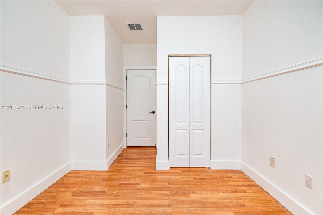 Interior space featuring wood-finish flooring, wainscoting detail, a solid-core interior door, and a two-panel bi-fold closet door