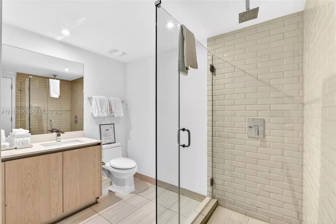 Walk-in shower featuring glass paneling, light-toned subway tile surround, and a ceiling-mounted rainfall showerhead, complemented by a wood-finish vanity with an integrated basin and a large rectangular mirror