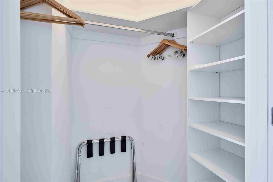Walk-in closet featuring white built-in shelving and a metal garment rod