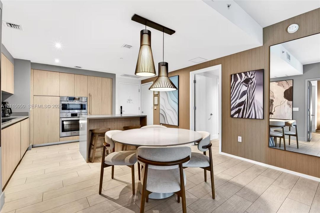 Kitchen featuring flat-panel wood-finish cabinetry, built-in stainless steel double wall ovens, a central island, modern pendant lighting, and wood-finish flooring