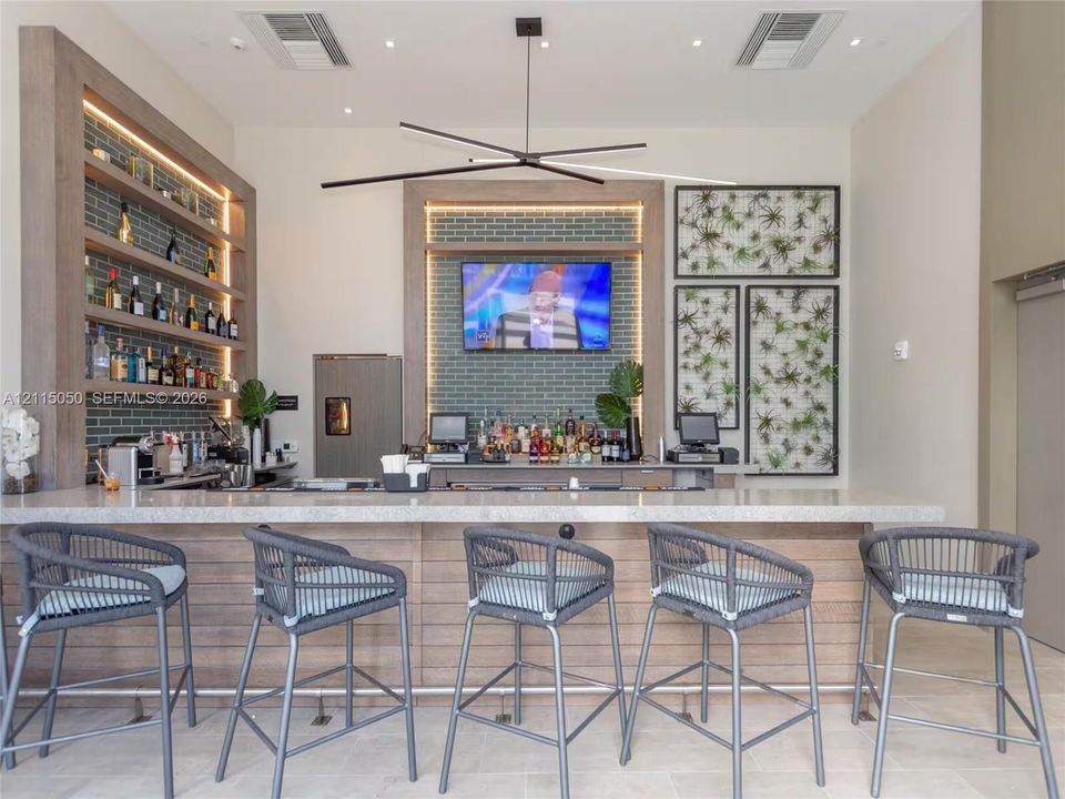 Built-in bar featuring a stone-composite countertop, wood-paneled base, integrated shelving with recessed lighting, and a linear modern pendant light fixture