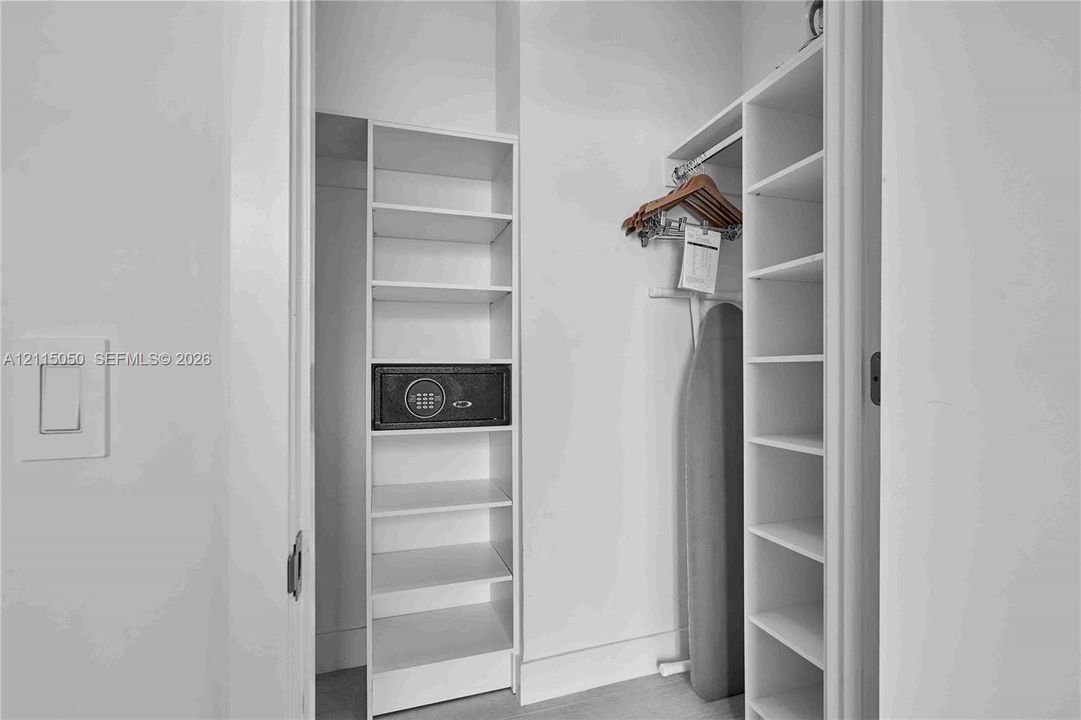 Storage closet featuring white built-in shelving, a dedicated recessed wall safe, and a metal hanging rod