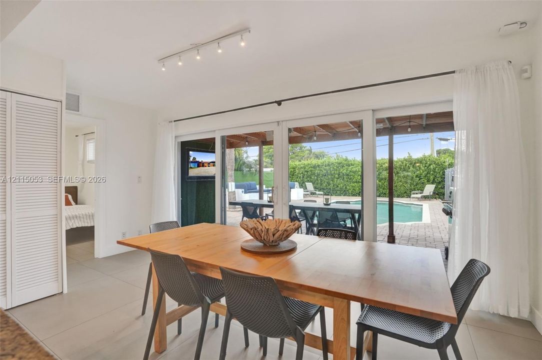 Large-format sliding glass doors, neutral tile flooring, louvered bi-fold closet doors, track lighting, and a paved outdoor patio area with a swimming pool