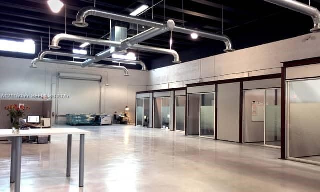 Open-concept industrial space featuring polished concrete flooring, exposed overhead ductwork, high ceilings, and modular office enclosures with sliding glass doors