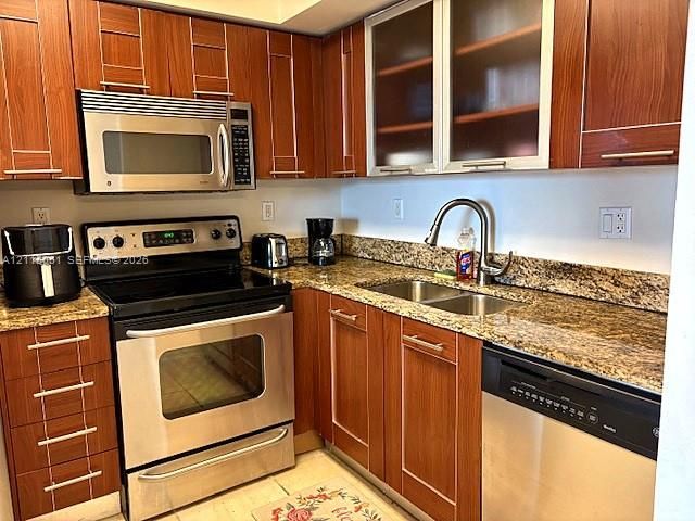 Kitchen featuring wood-finish cabinetry, stone countertops, stainless steel appliances, glass-front upper cabinet doors, and an arched-neck faucet