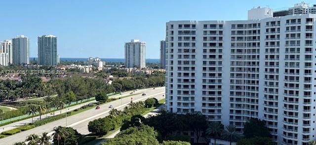 High-rise residential building featuring stacked private balconies, white facade, and surrounding mature landscaping