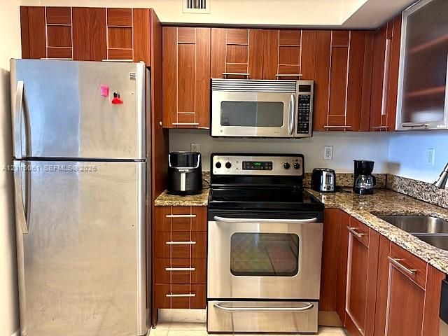 Kitchen featuring wood cabinetry, stone countertops, stainless steel refrigerator, stainless steel electric range, and stainless steel over-the-range microwave