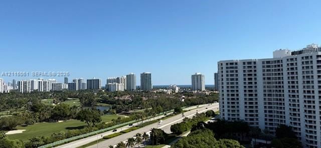 Elevated panoramic perspective showcasing expansive golf course grounds, mature perimeter foliage, and a backdrop of the coastal horizon and urban skyline