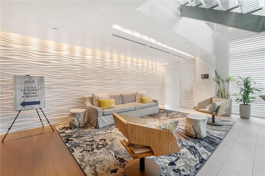 Textured, three-dimensional wave-pattern accent wall, high ceilings with integrated recessed lighting, metal-frame open-riser staircase, and floor-to-ceiling slatted window treatments