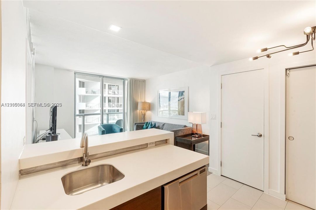 Kitchen featuring a white solid-surface countertop, stainless steel undermount sink with a gooseneck faucet, stainless steel dishwasher, modern multi-arm track lighting, and tile flooring