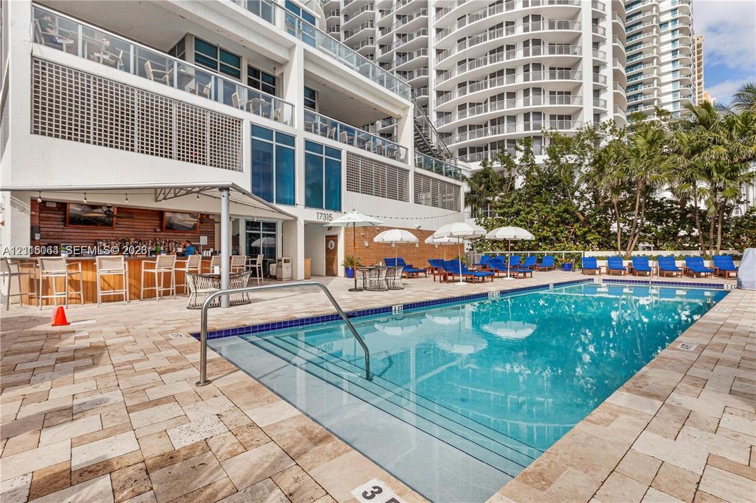 Swimming pool with tiled decking, built-in bar with wood-paneled walls, and structural balconies