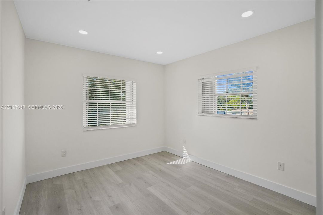 Neutral-toned interior featuring wood-finish flooring, recessed lighting, and dual windows with horizontal blinds