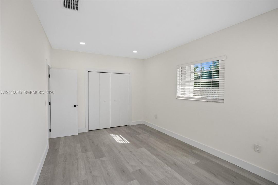 Neutral-toned interior featuring wood-finish flooring, recessed lighting, white walls, and a closet with bifold doors
