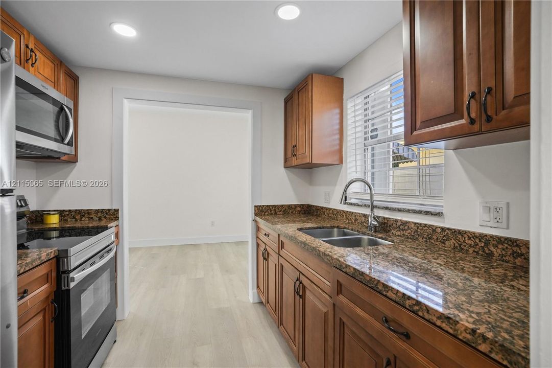 Kitchen featuring stained wood cabinetry, stone countertops, double-basin stainless steel sink, recessed lighting, and stainless steel appliances