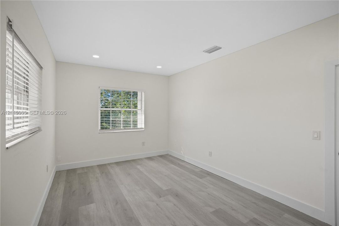Neutral-toned interior room featuring wood-finish flooring, recessed lighting, and multiple windows with horizontal blinds