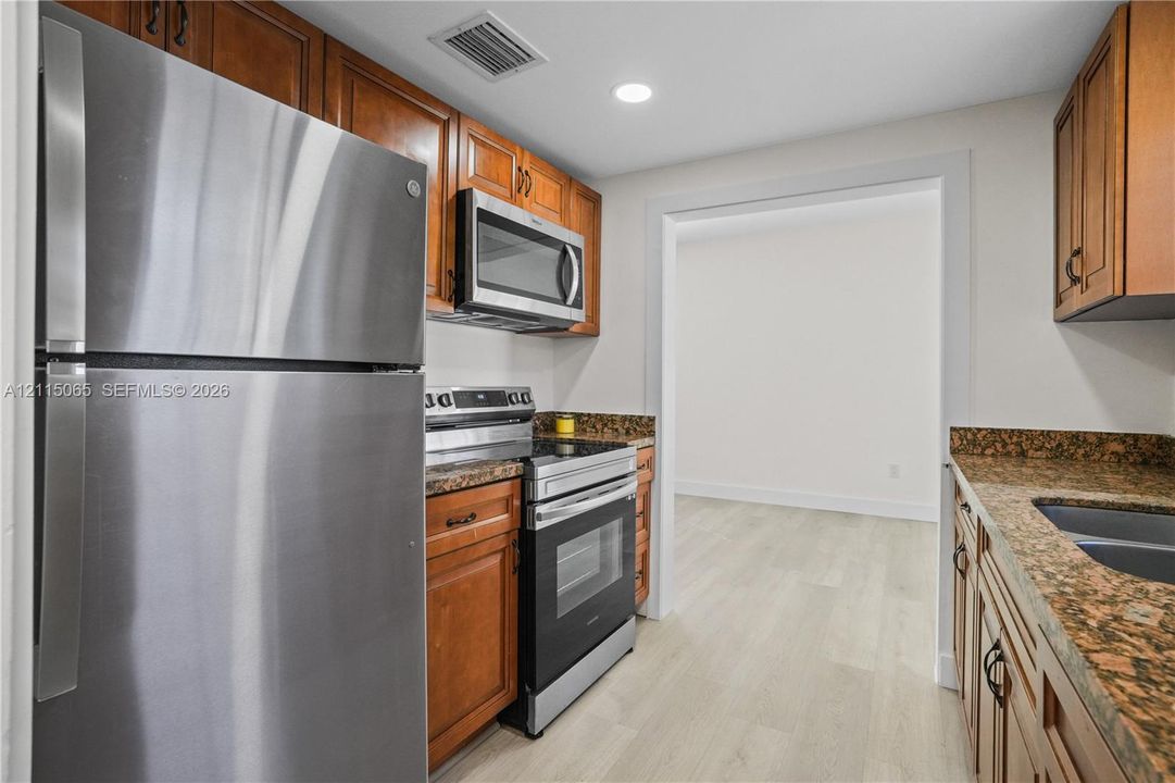 Kitchen featuring wood cabinetry, stone countertops, stainless steel appliances, and light-tone wood-finish flooring