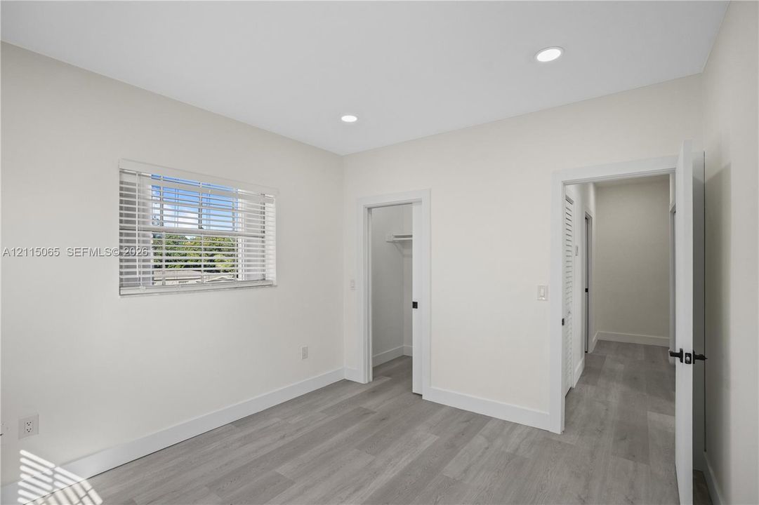Neutral-toned interior featuring wood-finish flooring, recessed lighting, a horizontal window with blinds, and built-in closet storage