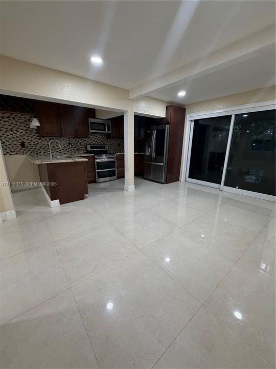 Kitchen featuring dark-toned cabinetry, stone-finish countertops, stainless steel appliances, decorative tiled backsplash, and large-format tile flooring with sliding glass doors