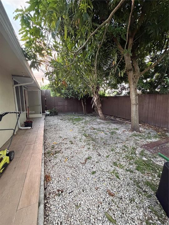 Exterior space featuring tile-surfaced patio, gravel landscaping, mature trees, and perimeter wood privacy fencing