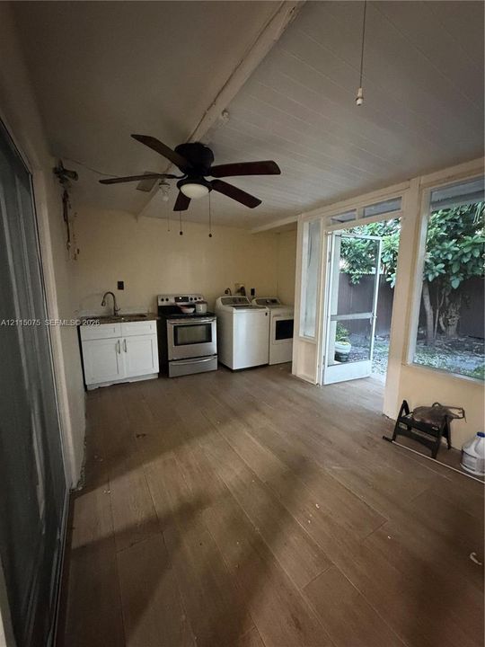 Multi-purpose utility space featuring wood-finish flooring, white cabinetry with a sink, a stainless steel range, and a ceiling fan