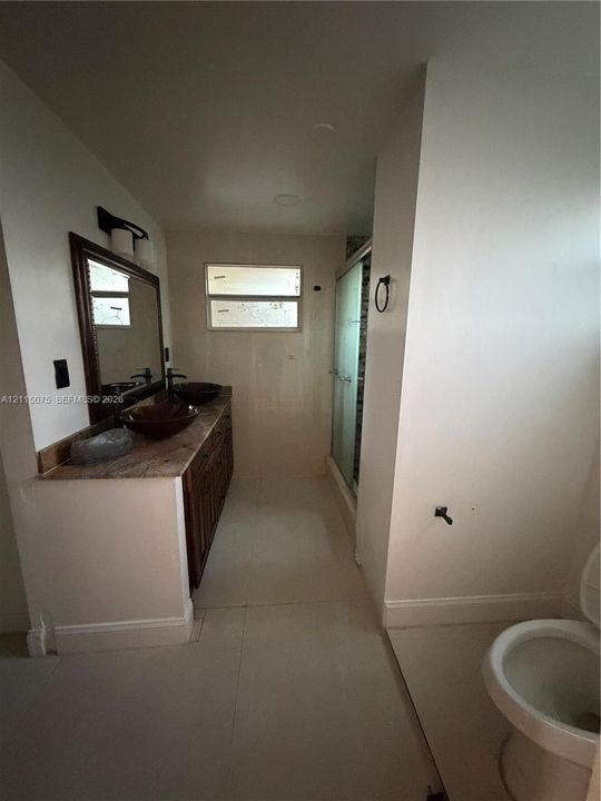 Bathroom vanity featuring dual dark-tinted glass vessel sinks, stone-finish countertop, wood-finish cabinetry, and a framed mirror