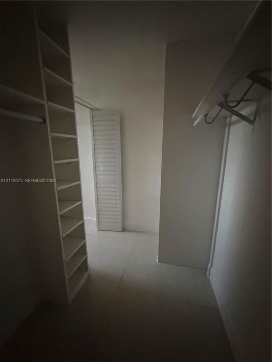 Walk-in storage space featuring built-in floor-to-ceiling shelving, overhead hanging rods, and a louvered door