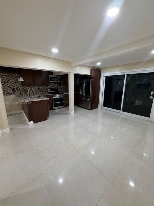 Kitchen featuring dark-finish cabinetry, stone-surface countertops, mosaic tile backsplash, stainless steel appliances, and large-format tile flooring