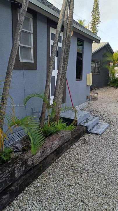 Exterior featuring stucco siding, timber-rail landscaping borders, concrete step entry, and gravel ground cover