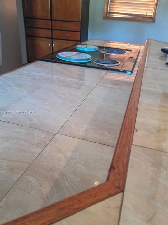 Tiled kitchen countertop with wood trim, integrated electric cooktop, and built-in cabinetry