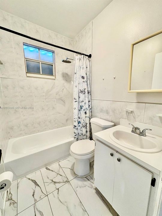 Bathroom featuring white vanity with integrated basin, polished metal faucet, white tile shower surround, and large-format patterned floor tile