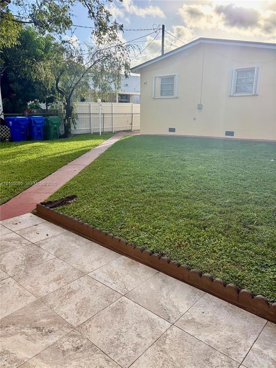 Rear exterior featuring a tiled patio, landscaped lawn, concrete pathway, and perimeter fencing