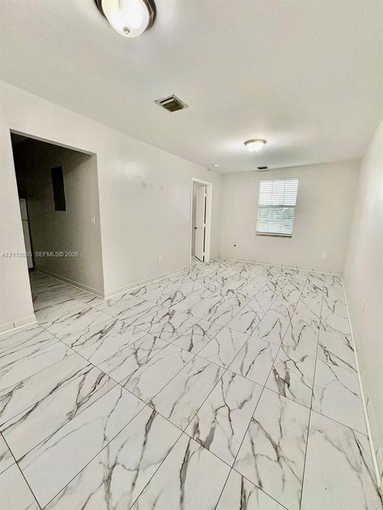 Neutral-toned interior space featuring large-format rectified tile flooring with a high-contrast veining pattern, flush-mount ceiling lighting, and a single window with slatted blinds