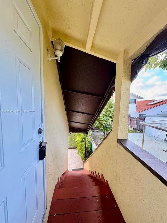 Exterior staircase featuring wood-finish treads, a metal awning, and a wall-mounted light fixture