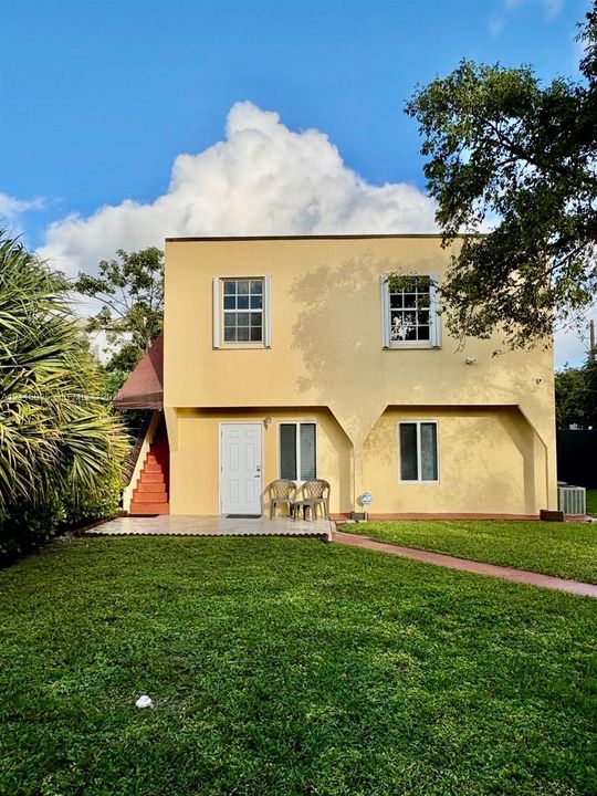 Two-story structure featuring stucco siding, arched architectural detailing, a paved ground-level patio, and exterior stairs