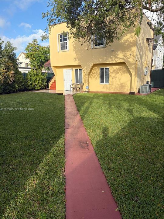 Two-story exterior featuring a stucco facade, multiple sash windows, a paved concrete walkway, and a spacious lawn