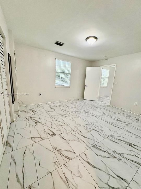 Large-format tile flooring with a veined pattern, louvered closet doors, and single-hung windows with blinds