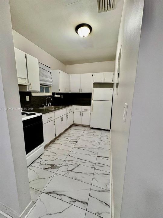 Kitchen featuring white shaker-style cabinetry, dark contrast backsplash, stainless steel sink, and large-format veined tile flooring